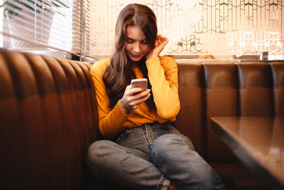 Teenage girl using smart phone while sitting in cafe