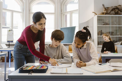 Teacher explaining male and female students sitting at desk in classroom