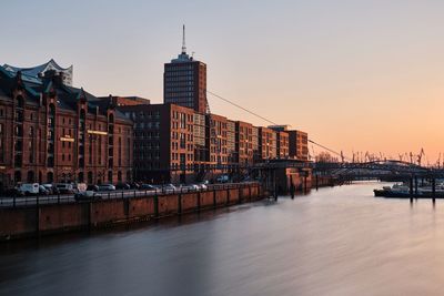 Residential buildings by river against clear sky during sunset