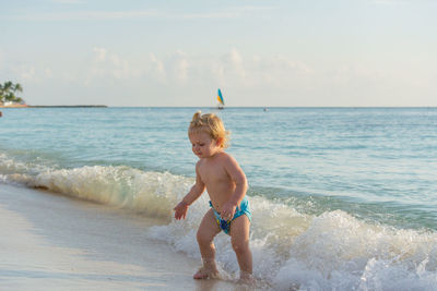 Full length of shirtless boy on beach against sky