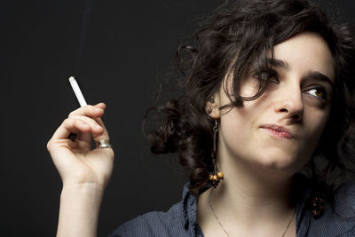 Portrait of young woman smoking cigarette against black background
