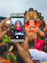 Cropped hands of woman photographing ganesh against sky