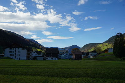 Houses on field by buildings against sky