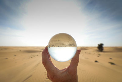 Person holding crystal ball on desert at against sky