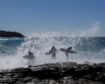 People with surfboards in sea against clear sky