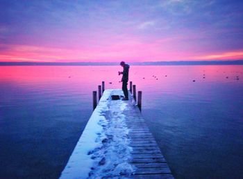 Man standing on pier amidst lake against sky during winter