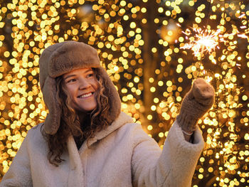 Portrait of young woman standing against illuminated christmas tree