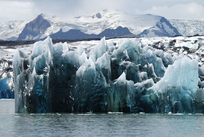 Scenic view of glacier in sea against snowcapped mountains