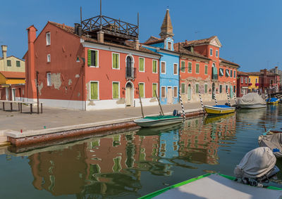 Boats moored at harbor by buildings against sky