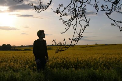 Man standing amidst plants on field against sky during sunset