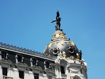 Low angle view of statue against building against clear blue sky