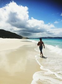 Full length of shirtless man standing on beach against sky