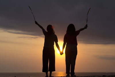 Silhouette people standing by sea against sky during sunset