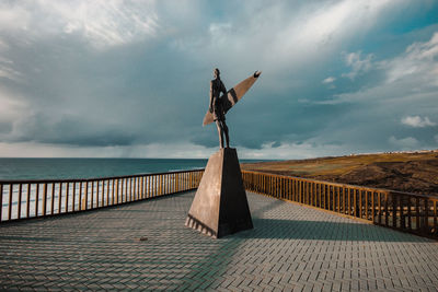 Man standing on railing by sea against sky