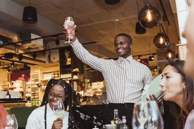 Smiling man holding wineglass by male and female friends during dinner party at bar