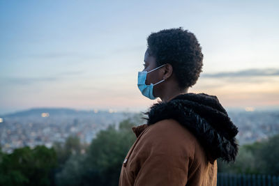 Portrait of young woman looking away in city against sky