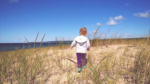 Rear view of girl walking at beach against blue sky