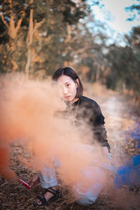Full length of woman holding distress flare while crouching in forest