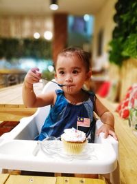 Baby girl eating cupcake while sitting on high chair