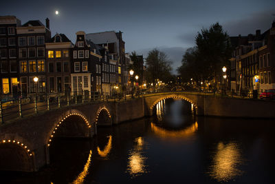 Illuminated bridge over river in city against sky at night