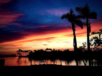 Silhouette palm trees by lake against romantic sky at sunset