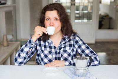 Woman drinking espresso on table at home