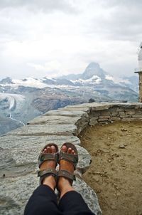 Low section of person on snowcapped mountains against sky