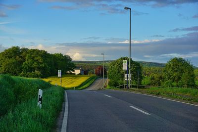 Road by trees on field against sky