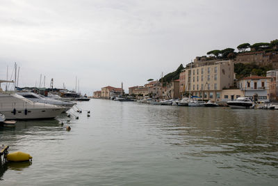 Sailboats moored in harbor by buildings against sky