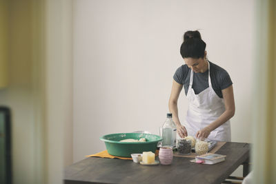 Young female preparing challah bread on table while standing against wall at home