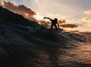 Silhouette men surfing against cloudy sky