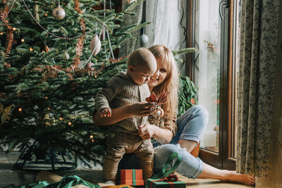 Happy mother playing with son in front of christmas tree