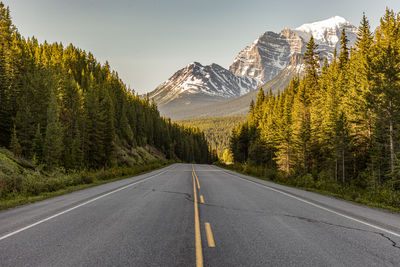 Empty road along trees and mountains against sky