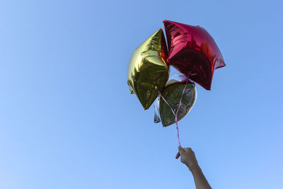 Cropped hand holding star shape helium balloons against clear blue sky