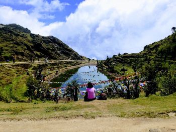 Rear view of young woman sitting on mountain against sky