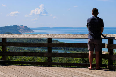 Rear view of man looking at sea against sky during summer