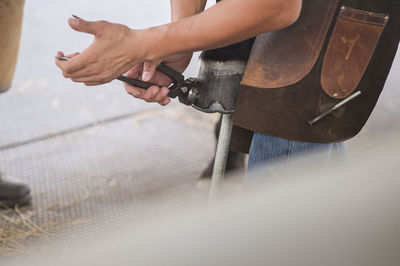 Midsection of farmer removing nail from horse leg