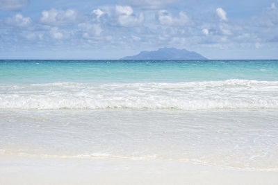 Tropical summer sea with smooth waves blue sky sand and lonely far island, tropical holiday concept