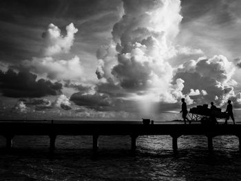 Silhouette people by sea against sky