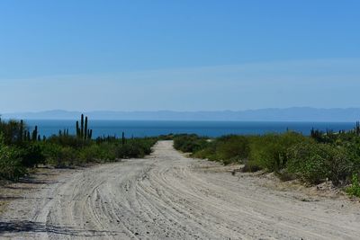 Dirt road by sea against blue sky