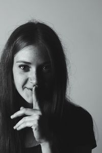 Portrait of young woman with finger on lips against wall