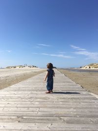 Full length of girl standing on boardwalk against sky