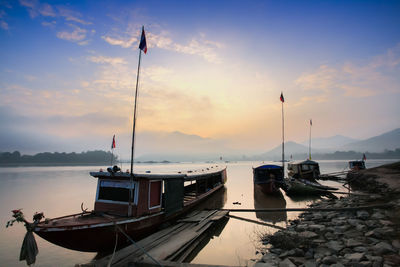 Sailboats moored on sea against sky during sunset