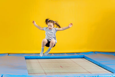 Full length of girl jumping against yellow wall