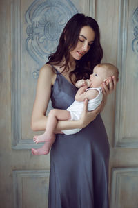 Mother in a nightgown holds a newborn boy in her arms at the window