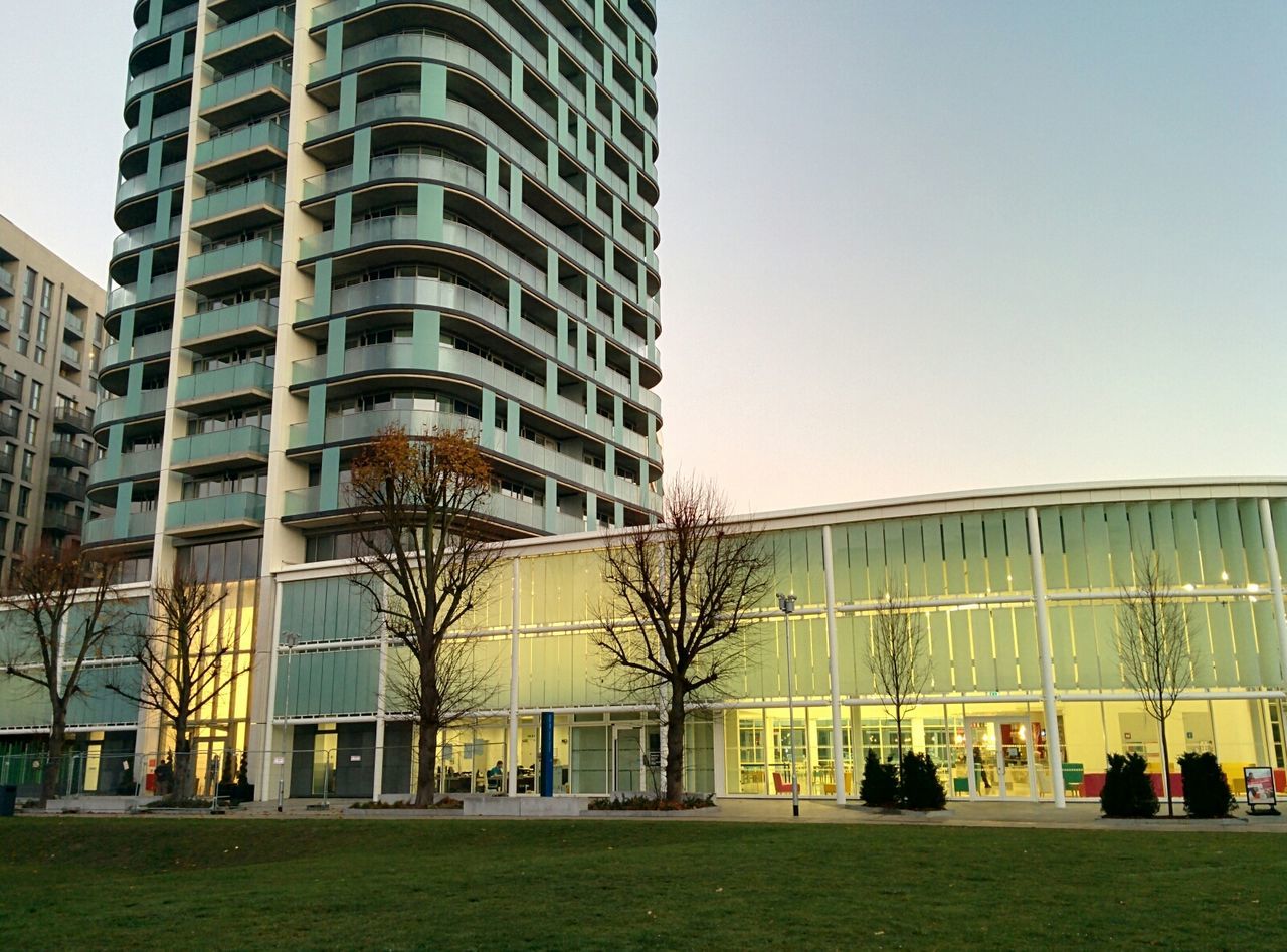 architecture, building exterior, built structure, clear sky, grass, city, modern, building, tree, office building, lawn, window, facade, city life, day, exterior, outdoors, incidental people, residential building, sky