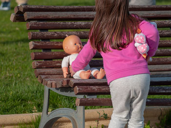 Rear view of girl holding doll on bench in park