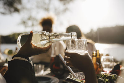 Cropped hand of woman pouring wine in glass for friend during dinner party