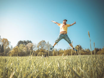 Low angle view of mature man jumping on grassy field against clear blue sky