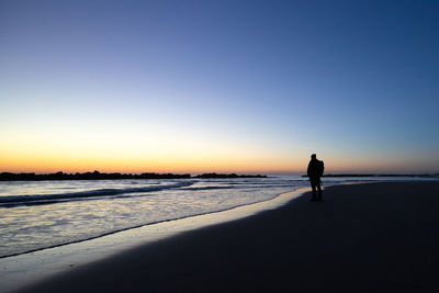 Silhouette man on beach against clear sky during sunrise